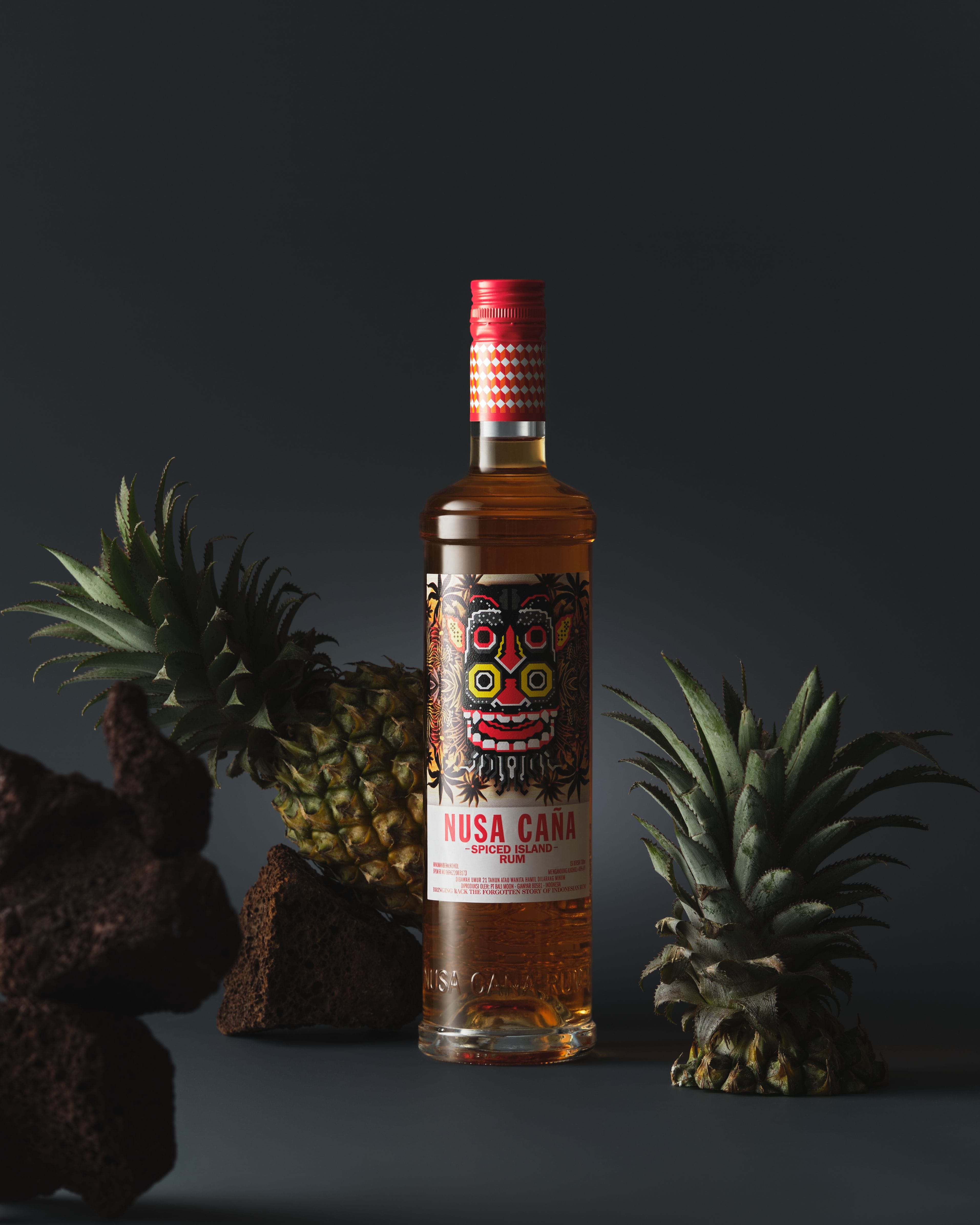 Nusa Caña Spiced Island rum bottle with a light charcoal background, lava rocks, and pineapples..